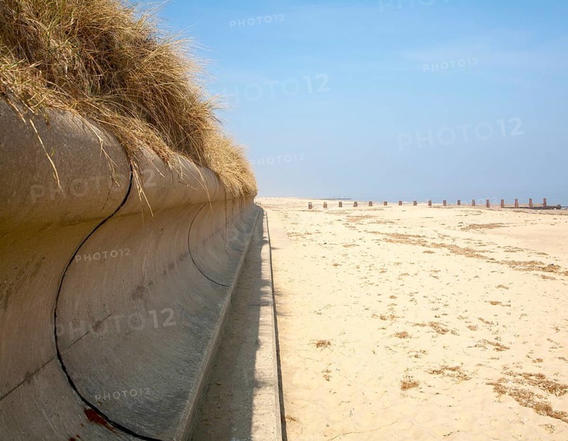 Wave return wall coastal defence and wide sandy beach submerging wooden groyne, Horsey, Norfolk, England, United Kingdom, Europe