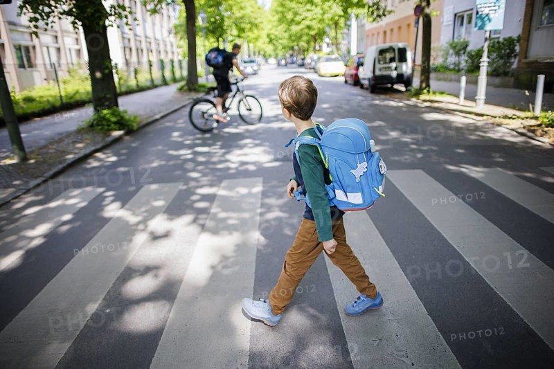 Symbol photo on the subject of schoolchildren in road traffic A six-year-old boy walks across the zebra crossing of a pedestrian crossing in front of a primary school with his school bag on his back. Berlin, 08.05.2024