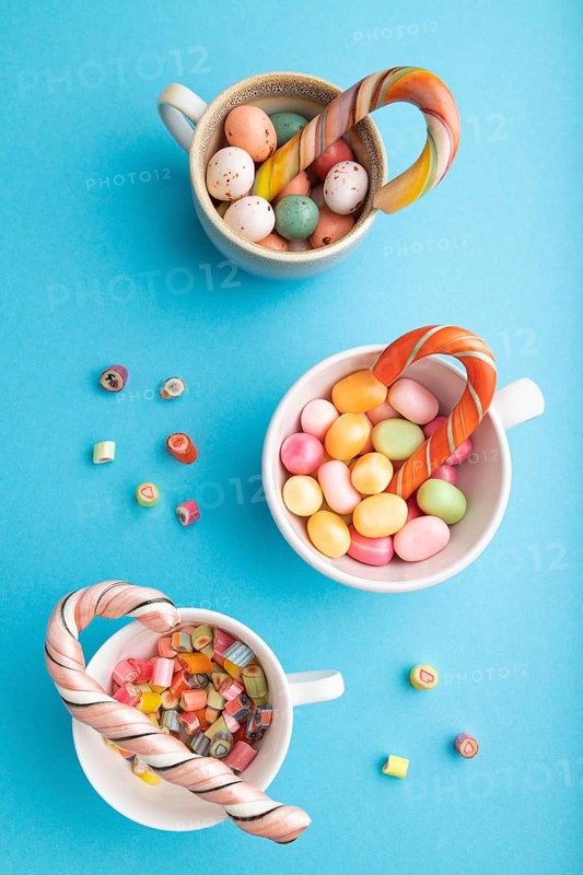 Heap of multicolored caramel candies in cups on blue pastel background. close up, top view, flat lay