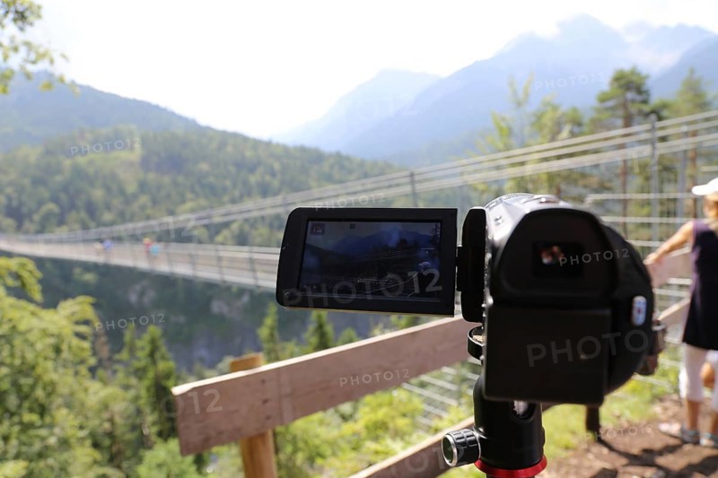 Close-up of a camcorder during video recording in nature. The mountains (Alps) and tourists can be recognised out of focus in the background