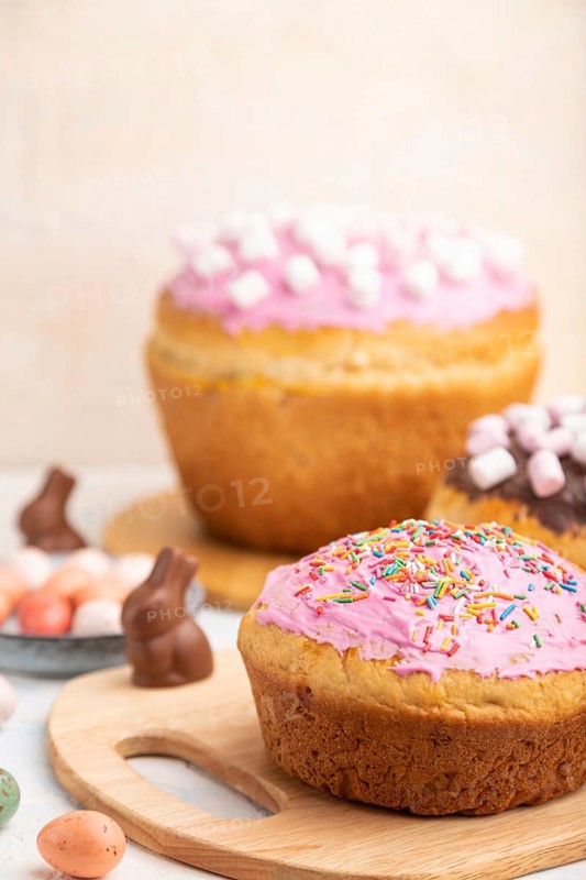 Homemade glazed and decorated easter pies with chocolate eggs and rabbits on a white concrete background and yellow textile. Side view, close up, selective focus