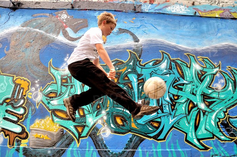 A ten-year-old boy plays with his football in front of a graffiti wall, football pitch in Germany
