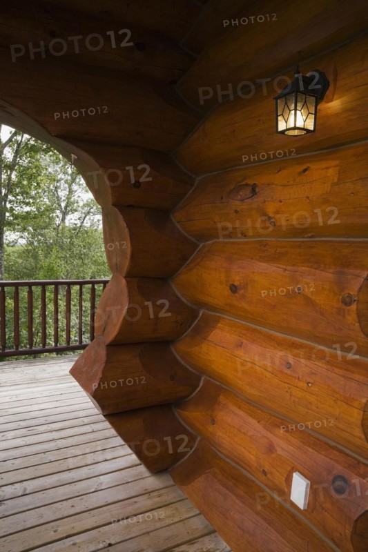 Brown reddish stained Scandinavian log cabin home with arch and wall made of large chinked logs and grey wood plank veranda in summer, Quebec, Canada, North America