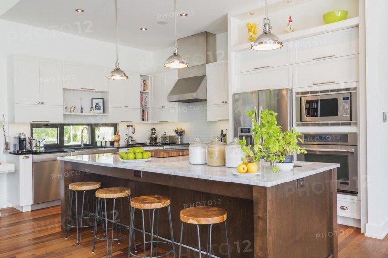 Kitchen area with white cabinets, marble top wooden island with painted black steel and exotic wood barstools, black granite countertops inside a luxurious modern cube style house, Quebec, Canada, North America