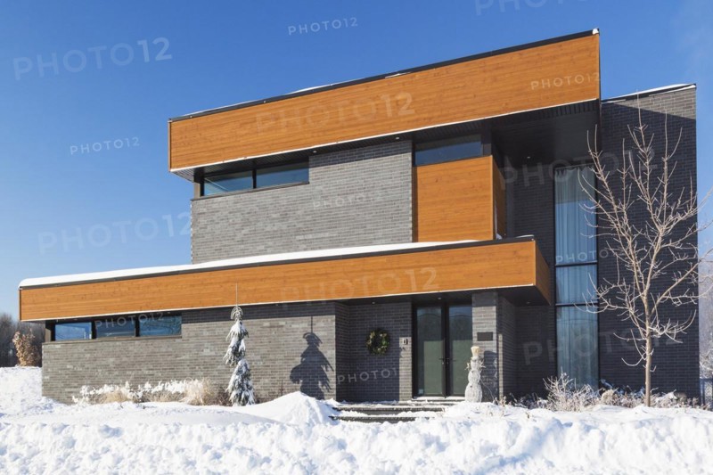Modern grey brick and stained wood finish cube style house facade with black trim in winter, Quebec, Canada, North America