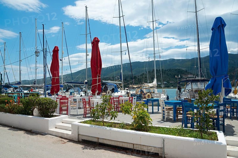 A harbour with moored boats and empty outdoor tables in front of mountains and a cloudy sky, Poros, Poros Island, Saronic Islands, Peloponnese, Greece, Europe