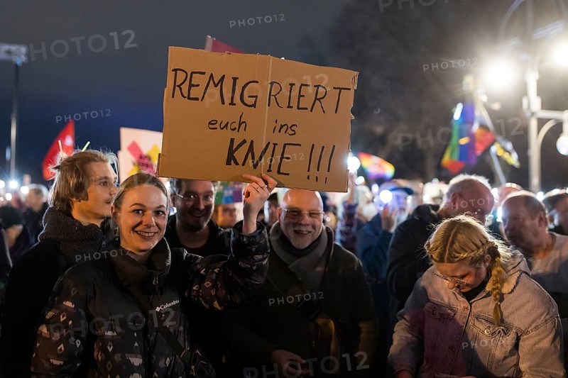 Participants with sign Remigrate yourselves to your knees!!! at the demonstration under the motto Sea of lights against the shift to the right in front of the Brandenburg Tor. The demonstration is directed against the general shift to the right in Germany by the AfD and CDU, among others, and in the USA by Donald Trump and Elon Musk, among others. Berlin, 25.01.2025