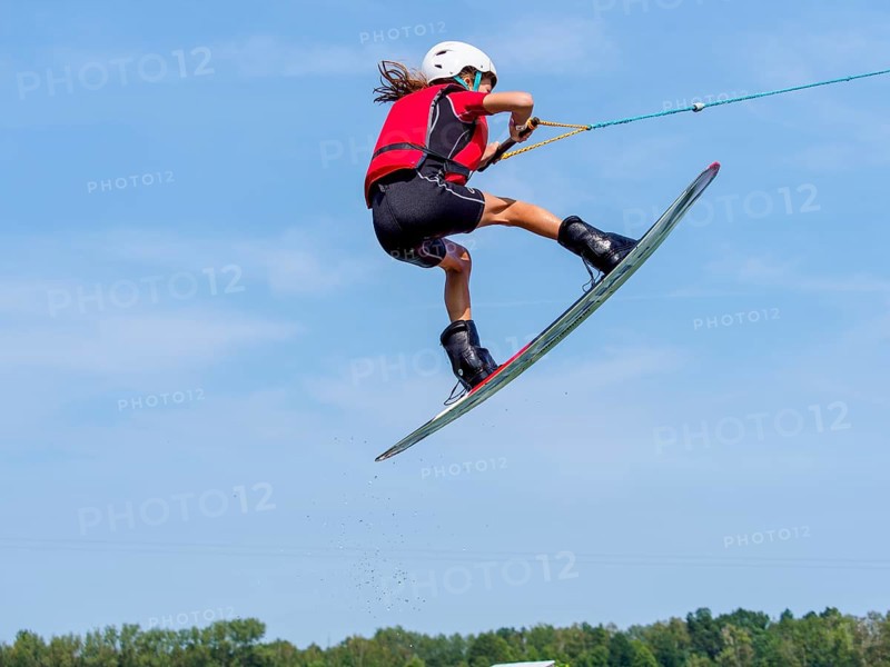 Boy or girl jumping with wakeboard, red life jacket, water sports, water skiing in wakepark
