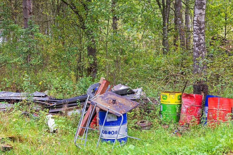 Environmental destruction with abandoned oil barrels and scrap metal in the forest