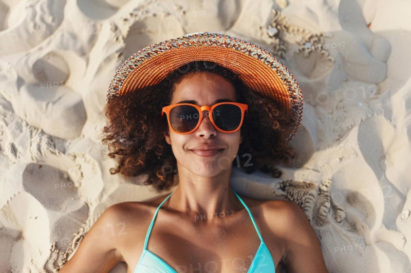 Young happy black woman with summer straw hat, sunglasses and swimwear lying in sand on beach. KI generiert, generiert AI generated