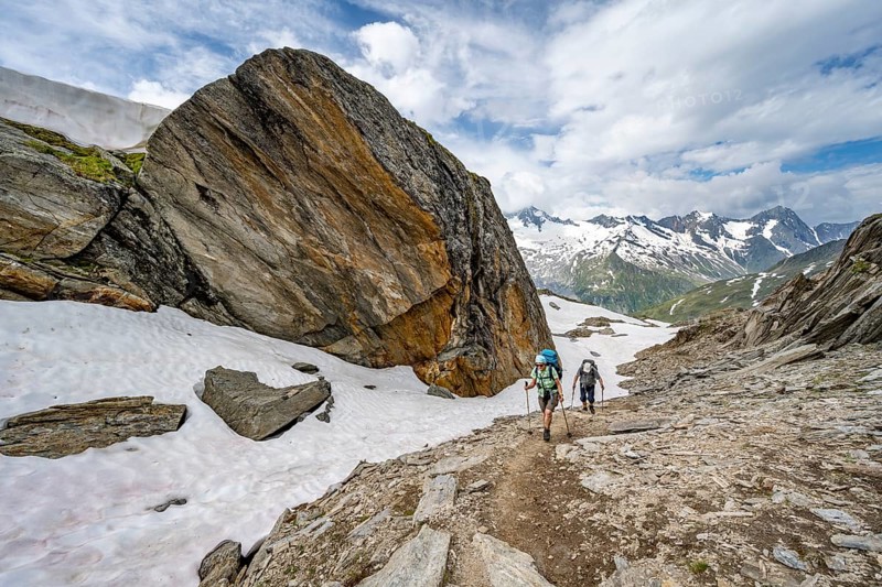 Mountaineer on a hiking trail next to a large boulder, ascent to the Nördliche Mörchnerscharte, mountain peak with snow and glacier in the background, Berliner Höhenweg, Zillertal Alps, Tyrol, Austria, Europe