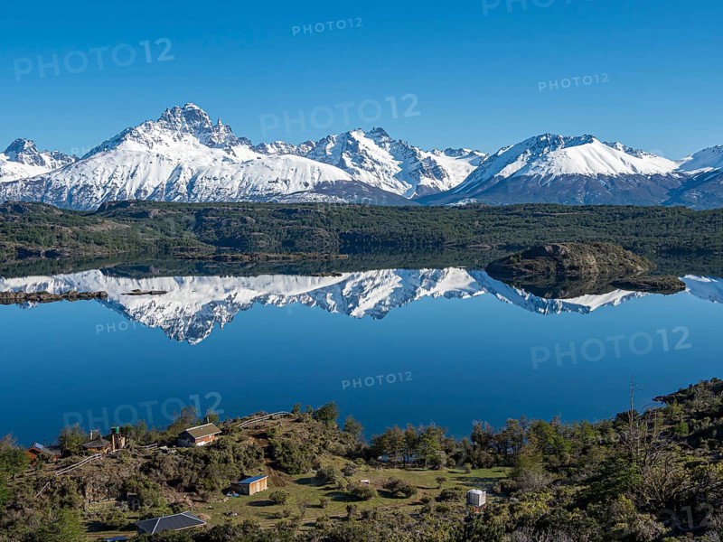 The snow-covered Mt. Cerro Castillo is reflected in a lake, small farm by the lake, Patagonia, Chile, South America