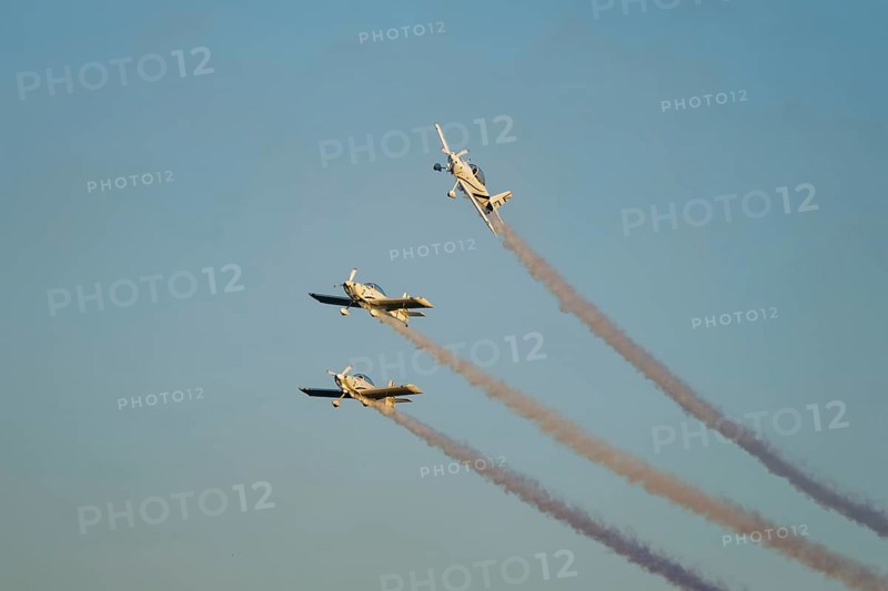 Three stunt aerobatic planes performing stunts in blue sky with smoke trail. Concept of teamwork, collaboration, coordination, trust, precision, difficulty, challenge, speed, synergy