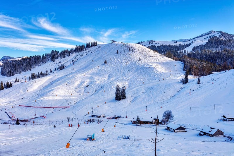 Snowy winter landscape with ski lift and huts against a clear blue sky, Sudelfeld