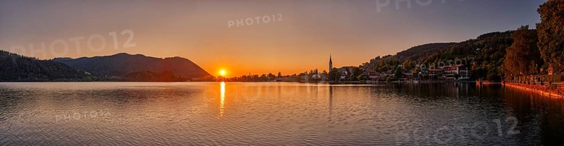 A peaceful sunset over a lake with mountains and a village in the background, Schliersee