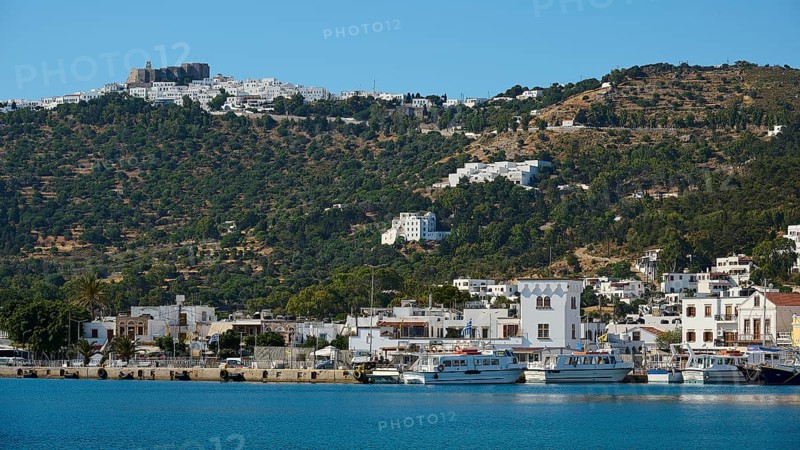 Coastal town with harbour, surrounded by white buildings, at the base of green hills and blue sky, Skala, Patmos, Dodecanese, Greek Islands, Greece, Europe