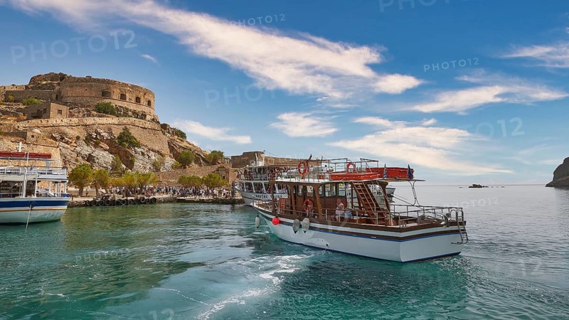 A white boat lies in a quiet harbour near a historic fortress under a blue sky, Venetian Sea Fortress, Leper Island, Spinalonga, Elounda Bay, Mirabello Bay, East Crete, Crete, Greek Islands, Greece, Europe