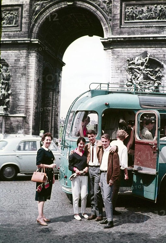 Three young people two men a woman standing by open bus door entrance older woman nearby, Arc de Triomphe, Paris, France c 1960