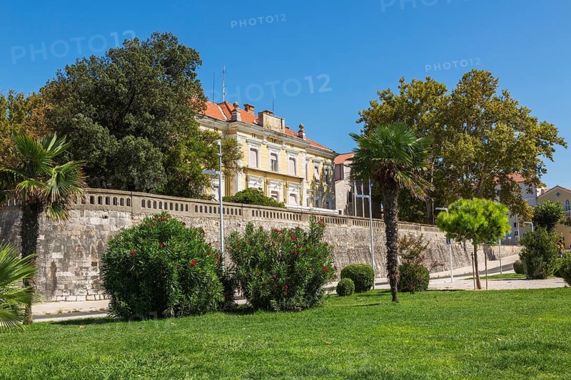 Landscaped park with green grass lawn and old yellow architectural building with terracotta clay roof tiles housing the Zadar County Offices in late summer, Zadar, Croatia, Europe