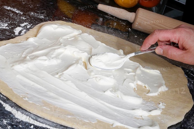 Swabian cuisine, preparation of savoury yeast plait with smoked meat, salty wreath bread, yeast yeast dough pastries, spread raw yeast dough with sour cream, behind rolling pin, grandmother's kitchen, regional, home cooking, typical Swabian cuisine reinterpreted, traditional cuisine reinterpreted, men's hands, food photography, studio, Germany, Europe