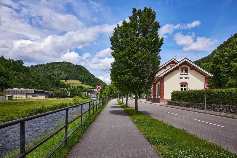River Kinzig, metal railing, footpath and cycle path, trees, historic railway station building, Offenburg Ortenau GmbH music school, Wolfach town band, hilly landscape, coniferous forest, blue sky, cumulus clouds, Bahnhofstraße, Wolfach, Black Forest, Ortenaukreis, Baden-Württemberg, Germany, Europe
