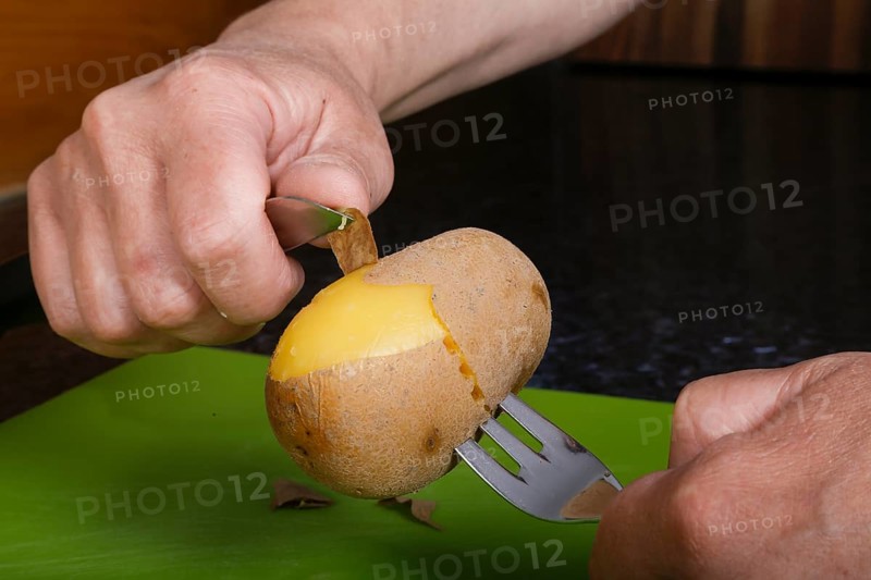 Swabian cuisine, preparation of Swabian potato salad with Stuttgarter Leberkäs in a horseradish-mustard coating, peeling boiled potatoes, jacket potato, grandmother's kitchen, regional, home cooking, typical Swabian, fork, knife, men's hands, traditional cuisine, food photography, studio, Germany, Europe