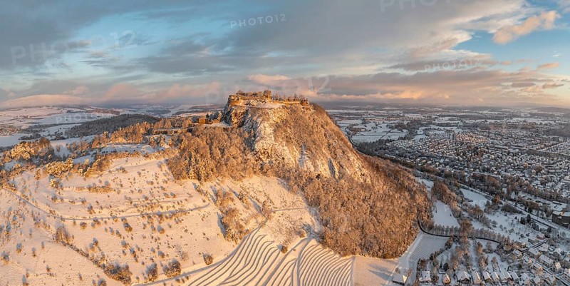 Aerial view, panorama of the snow-covered Hegau volcano Hohentwiel with Germany's largest castle ruins on a cold winter morning, at sunrise, in front of it Germany's highest vineyard, the Elisabethenberg at 505 metres above sea level, on the right the town of Singen, district of Constance, Baden-Württemberg, Germany, Europe