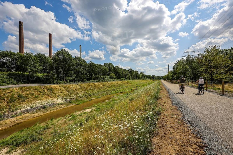Bottrop, North Rhine-Westphalia, Germany, Renaturalised Boye, the tributary of the Emscher, was transformed into a near-natural body of water, flood protection through newly designed floodplains, the Boye is now free of wastewater after the construction of a parallel sewer, is part of the Emscher river system and thus part of the Emscher conversion, was previously an open, above-ground wastewater canal, mixed water canal with surface water and wastewater. Left Industrial area with chimneys on Essen territory. New cycle path on the right, Europe