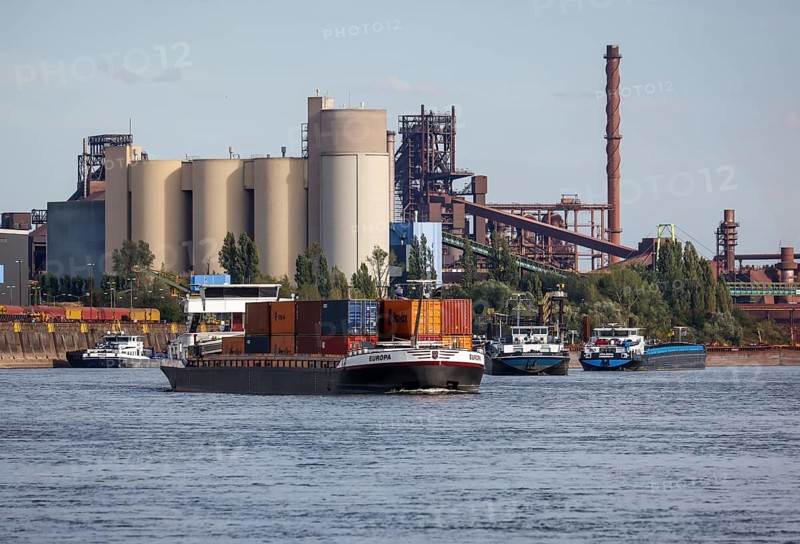 Duisburg, North Rhine-Westphalia, Germany, freighter at the southern harbour, Holcim cement works at the rear left, ThysseKrupp Steel blast furnace Schwelgern in Duisburg Marxloh at the rear right. Due to the draught, freighters can only navigate the Rhine with a small load and sometimes park in front of the entrance to Duisburg harbour due to the low water level, Europe