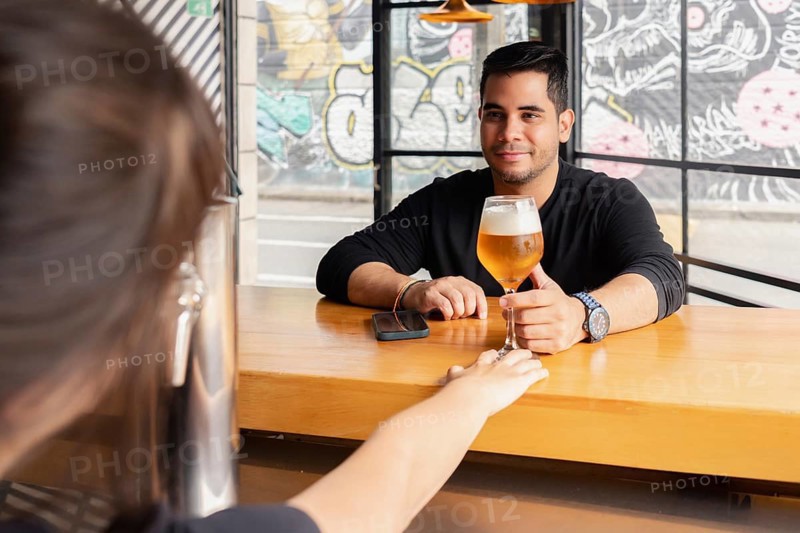 A man smiles as he receives a freshly poured beer from a bartender at the bar of a contemporary bar