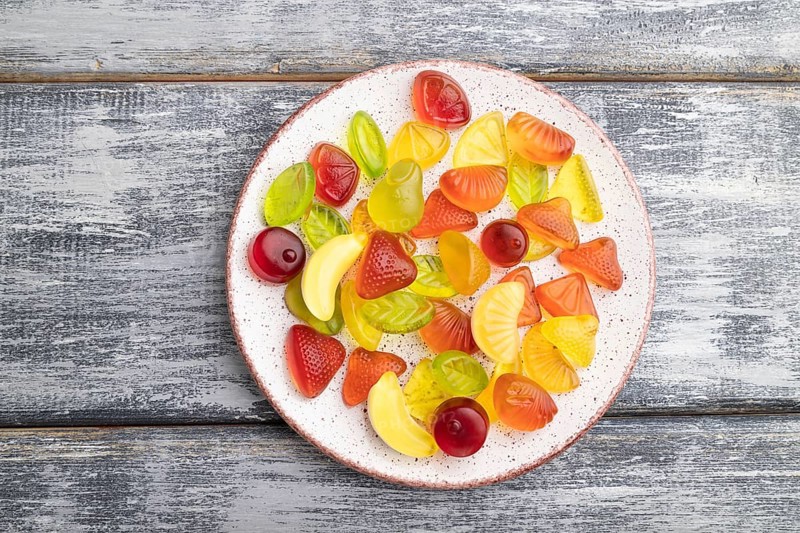 Various fruit jelly candies on plate on gray wooden background. top view, flat lay, close up