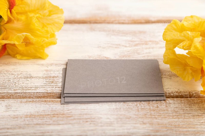 Gray business card with iris yellow flowers on white wooden background. side view, copy space, mockup, template, spring, summer minimalism concept