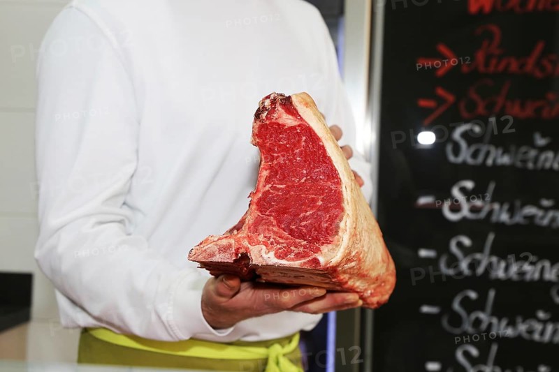 Butcher holds a dry aged T-bone steak in his hand