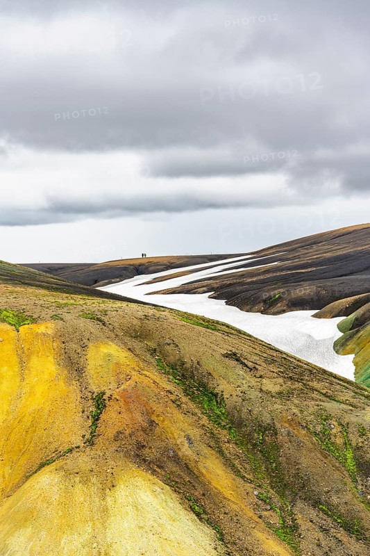 Two hikers on a hill in the distance, colourful volcanic landscape with hills and snow, Laugavegur trekking trail, Landmannalaugar, Fjallabak Nature Reserve, Icelandic Highlands, Suðurland, Iceland, Europe