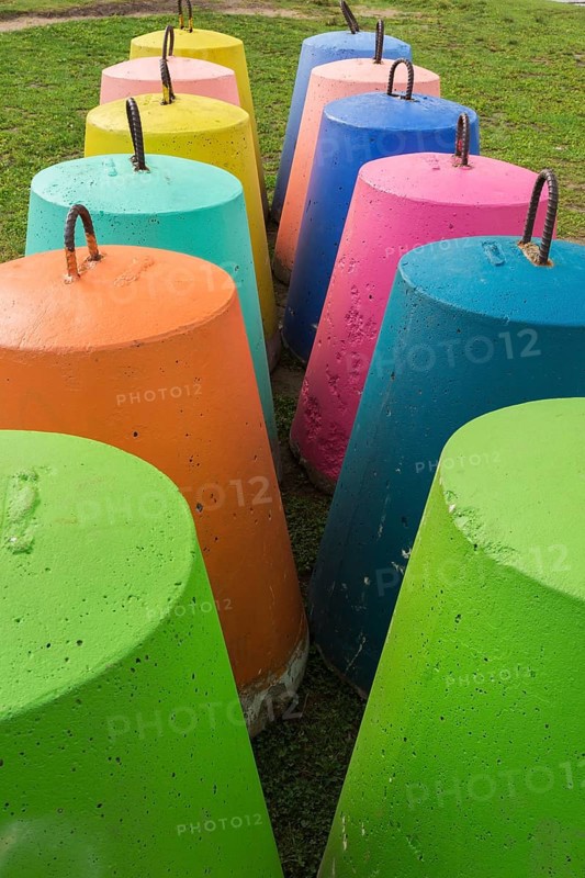 Two rows of fluorescent green, orange, blue, pink, turquoise and yellow painted bell shaped concrete blocks with steel handles on grass lawn in public park in summer, Quebec, Canada, North America