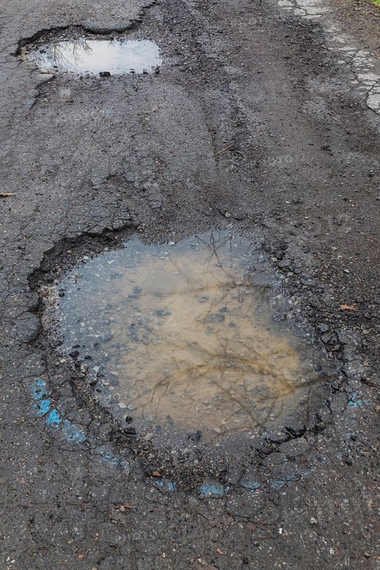 Potholes filled with rainwater on wet black asphalt road surface in spring, Montreal, Quebec, Canada, North America