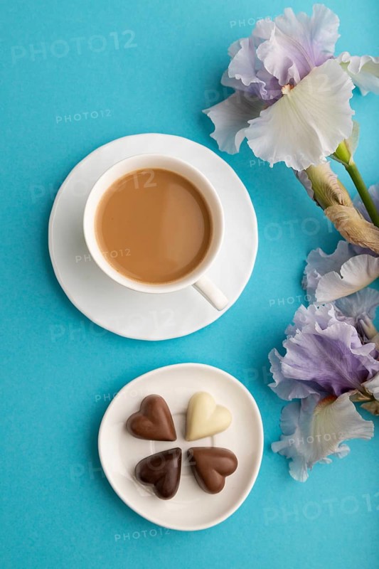 Cup of cioffee with chocolate candies and lilac iris flowers on blue pastel background. top view, flat lay, close up, still life. Breakfast, morning, spring concept