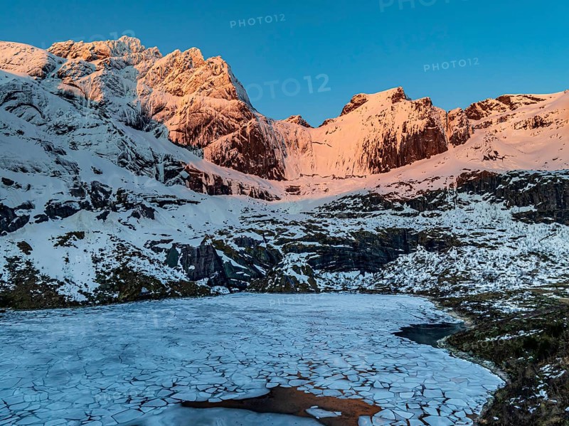 Aerial view of icy lake in front of steep mountains, winter, sunrise, Storvatnet, Flakstadoya, Lofoten, Norway, Europe