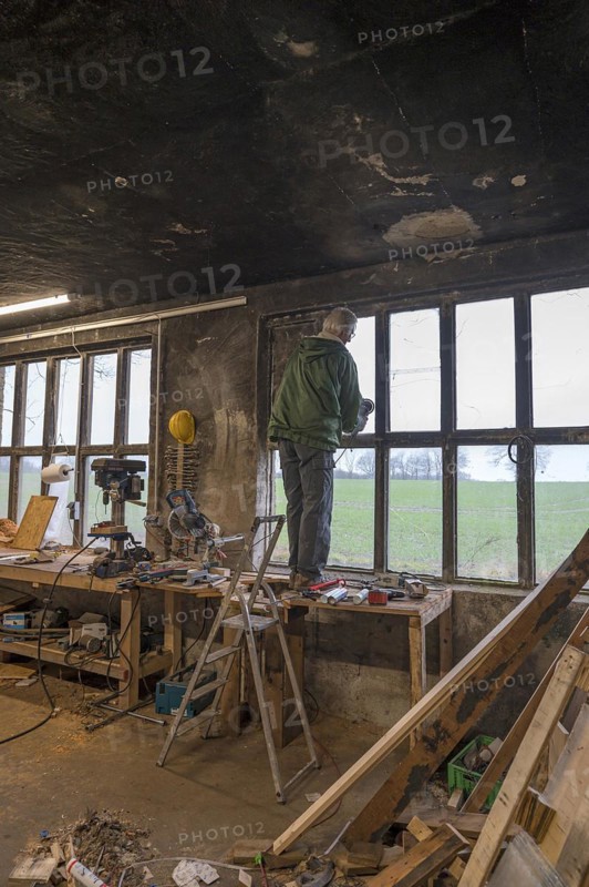 Elderly man standing on a workbench and repairing a window in a workshop, Mecklenburg-Vorpommern, Germany, Europe