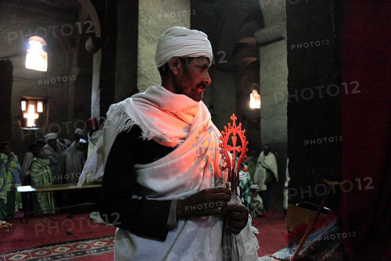 Rock churches of Lalibela, the World Reader's Church, Pray Medhane Alem, House of the World Reader, Pilgrim prays with Ethiopian Orthodox cross in the church, Ethiopia, Africa