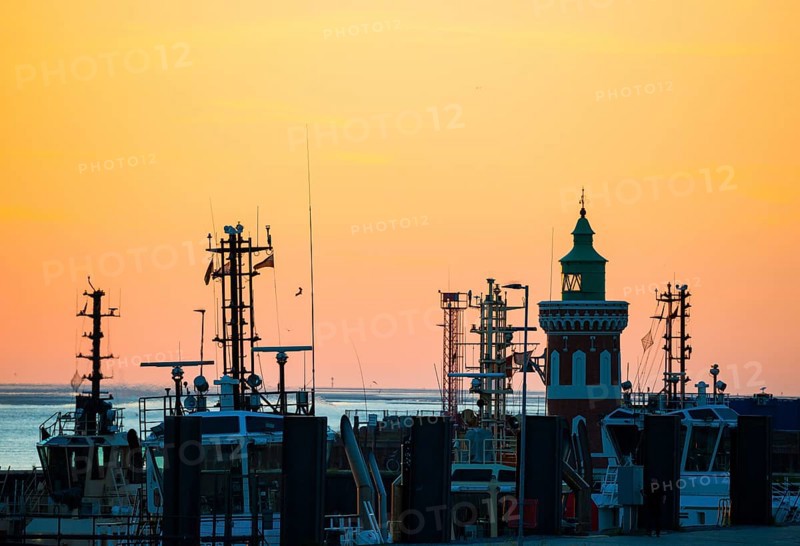 Harbour at sunset with various boats and the sea in the background, the sky in bright orange, Pingelturm, historic lighthouse behind harbour facilities with ships, cutter, twilight, evening, dusk, maritime, calm atmosphere, mouth of the Weser into the North Sea, Outer Weser, coast, Bremerhaven, Land Bremen, Germany, Europe