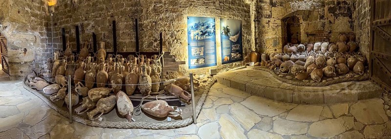 Panoramic photo of view of ancient amphorae from wreck recovered in Mediterranean Sea sunken sea exhibited in 16th century fortress built by Republic of Venice old name Castello Rocca al Mare today Koules in harbour of Iraklion today museum, in the middle background display board with explanation of salvage underwater by divers at underwater archaeology, Heraklion, Crete, Greece, Europe