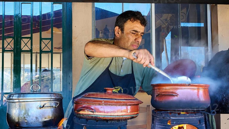 Chef Stelios, A man stirs in a pot on an open fire in a rustic kitchen while other pots stand next to him, Drakona, Slowfood, Restaurant Dounias, Lefka Ori, White Mountains, Mountain massif, West, Crete, Greece, Europe