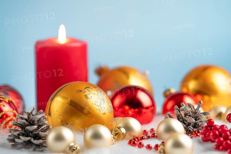 Burning candle with red and gold baubles and pine cones on artificial snow, festive atmosphere