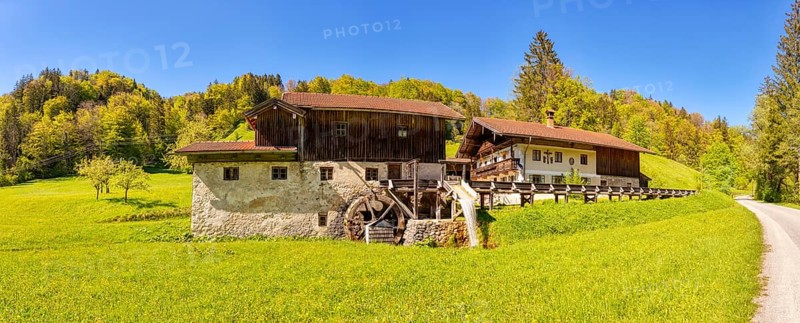 A picturesque watermill in the middle of a green landscape with a blue sky and forest in the background, Nussdorf Mühle