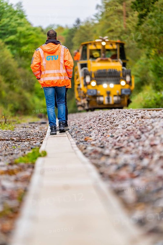 A man in an orange jacket walks along a railway line, a yellow tractor follows, track construction Hermann Hesse Bahn, district of Calw, Black Forest, Germany, Europe