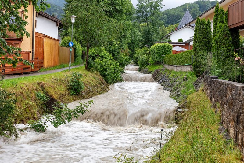 Small stream in a residential area with a strong current, surrounded by green trees and houses, Osterbach, Bad Feilnbach