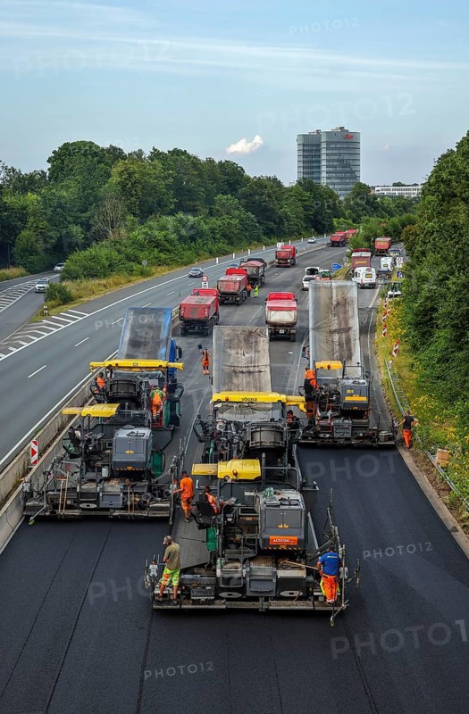 Essen, North Rhine-Westphalia, Germany, road construction, asphalt pavers and road rollers laying new, open-pored, whisper asphalt on the A52 motorway, here between the Essen-Kettwig and Essen-Rüttenscheid junctions in the direction of Dortmund. Skyline of Essen with the EON headquarters building in the background, Europe