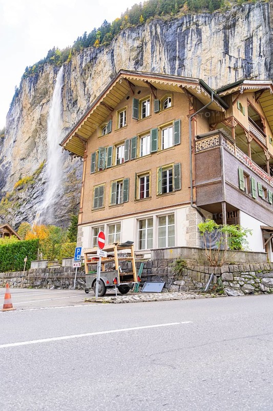 Traditional house in front of a waterfall, with a road in the foreground, Lauterbrunnen, Switzerland, Europe