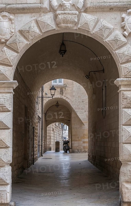 Stone arch above a narrow cobbled alley with antique lamps and historic stone walls, Altamura historic centre, Apulia, Italy, Europe